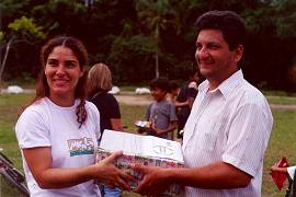 A autora do projeto, Caroline Roldam, entrega um dos pacotes de livros ao presidente da Sociedade de Melhoramentos, Wagner Mem de S�